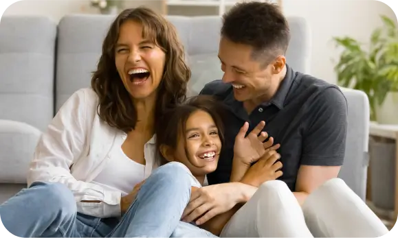 Familia de tres personas abrazadas, dos adultos jóvenes y una niña, felices en referencia a los seguros de hogar de Seguros Caracas