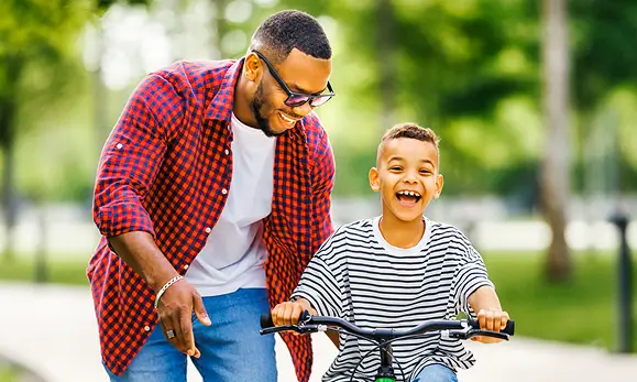 Padre enseñando a su hijo a manejar bicicleta felices en referencia a la Póliza de Seguro de Accidentes Personales Individual de Seguros Caracas